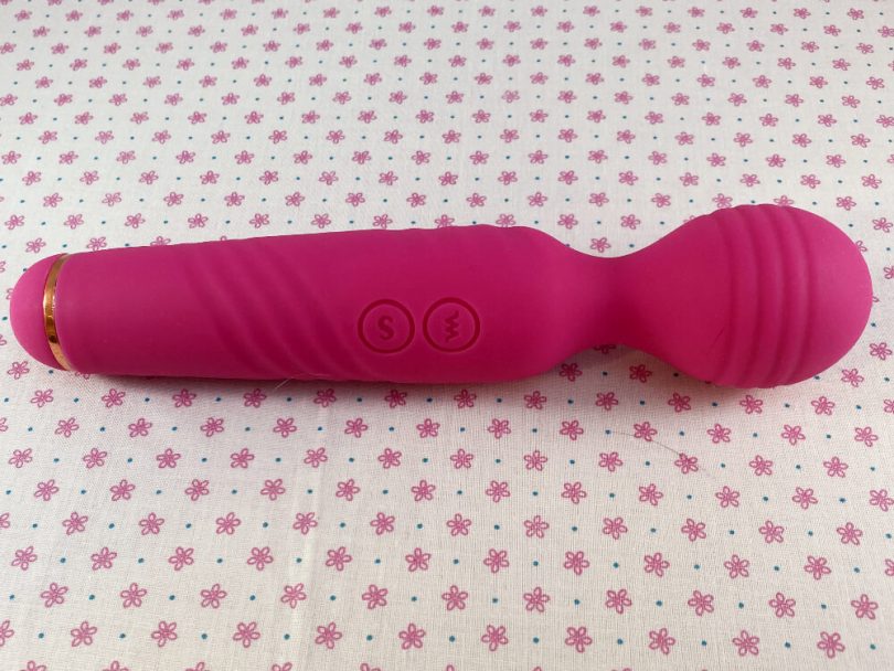 Side view of Sucking Clitoral Stimulator and Wand Massager by Sohimi -- hot pink vibrator on top of fabric with pink flowers and white background
