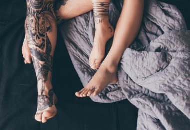 tattoed legs of man and woman in bed with rumpled blankets